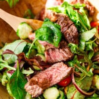 Steak salad being tossed with wooden salad tongs.