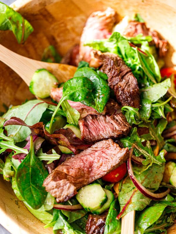 Steak salad being tossed with wooden salad tongs.