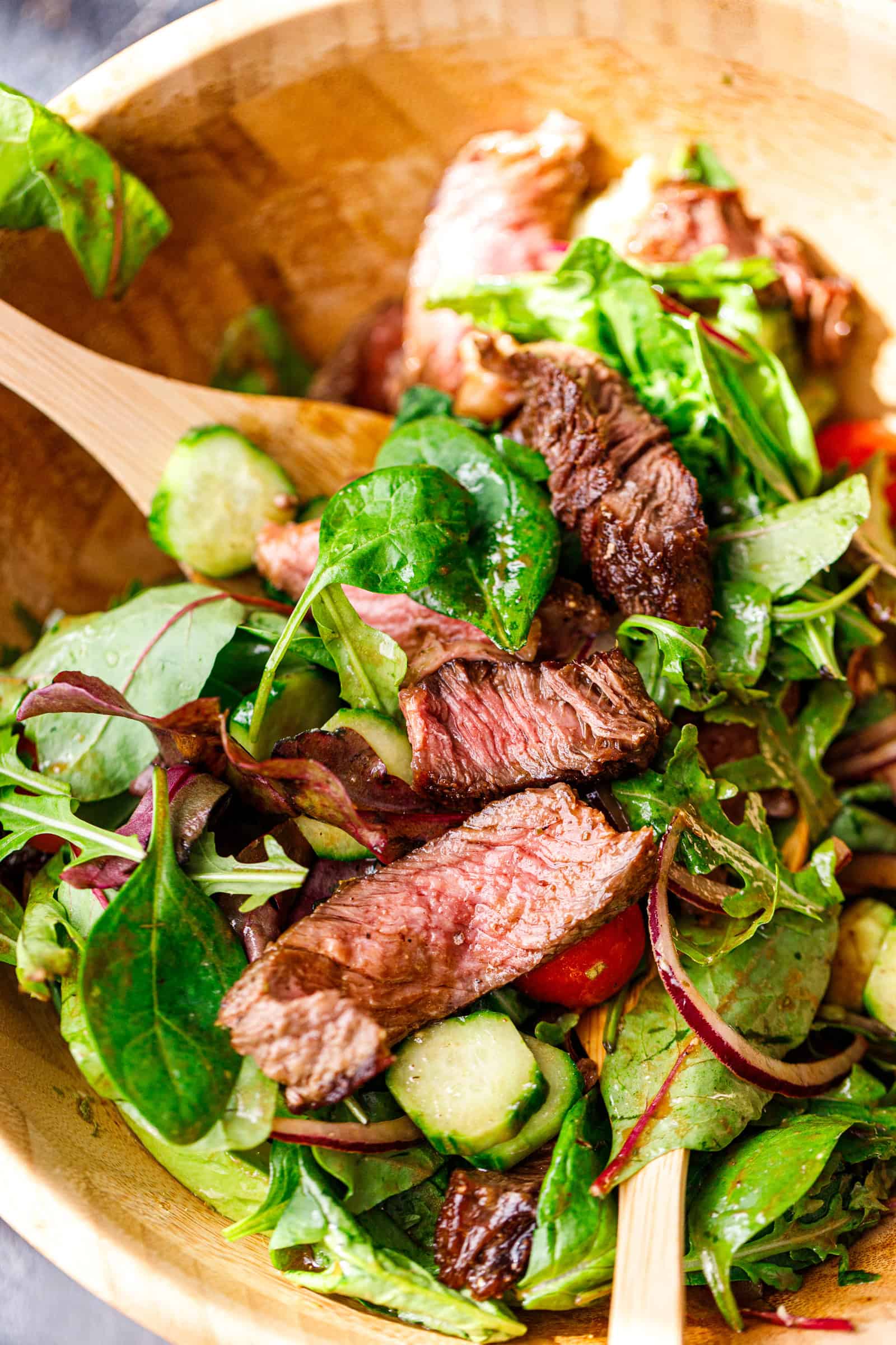 Steak salad being tossed with wooden salad tongs.