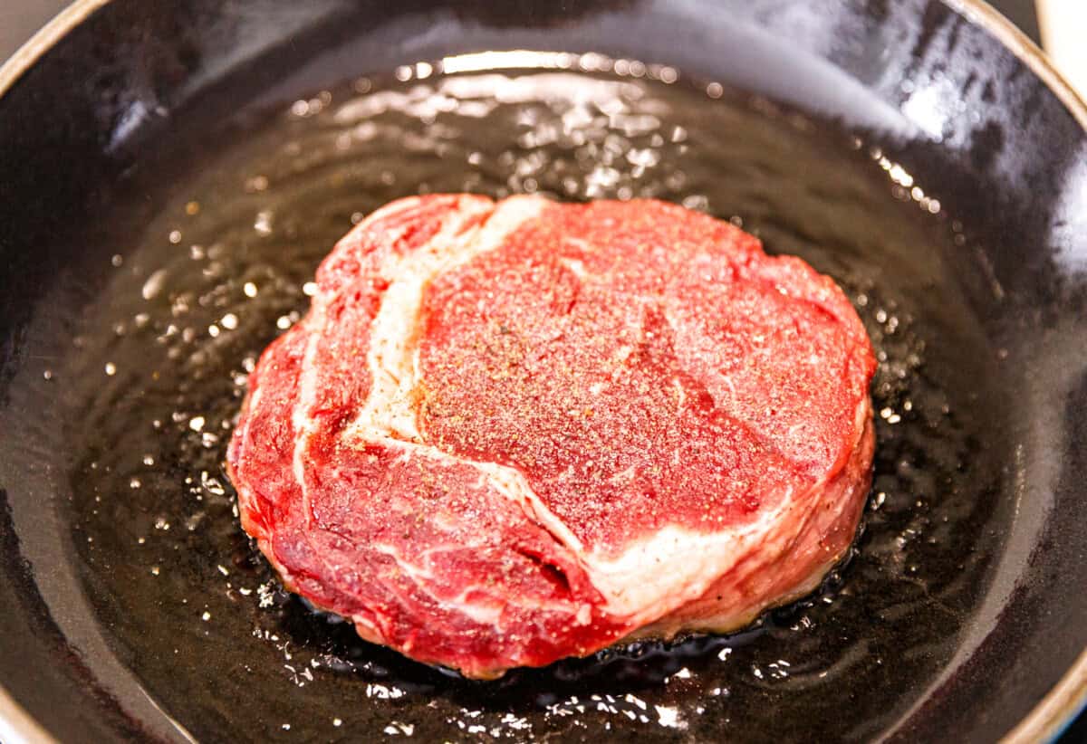 Seasoned steak searing in a hot skillet with olive oil.