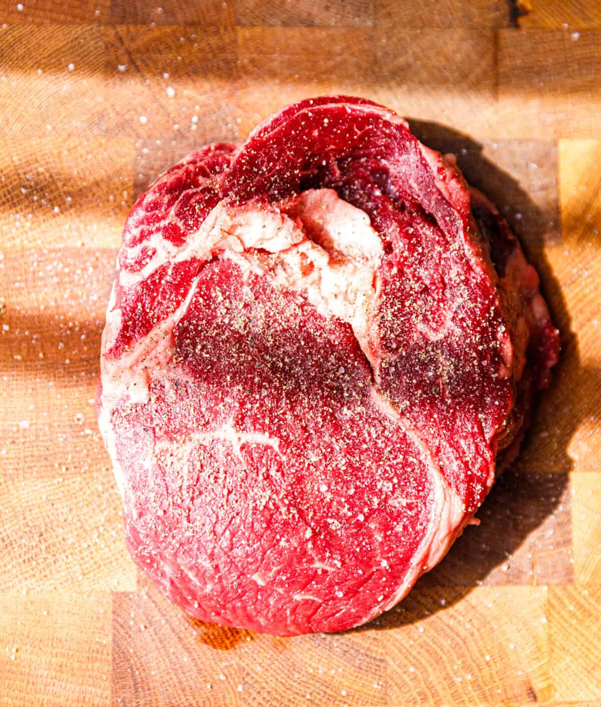 Raw ribeye steak on a wooden cutting board, ready for seasoning.