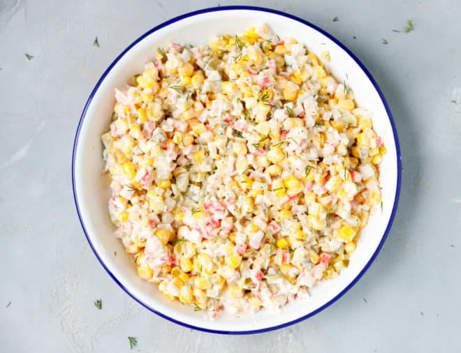 A bowl filled with a salad made of crab meat, pickles and corn
