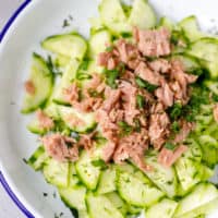 A white bowl with blue rim and tuna cucumber salad inside