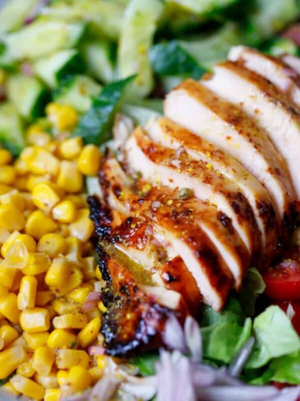 Honey mustard chicken breast sliced in a bowl with greens and corn