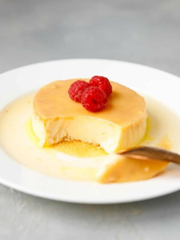 Keto Flan (creme Caramel) on a white plate, topped with raspberries