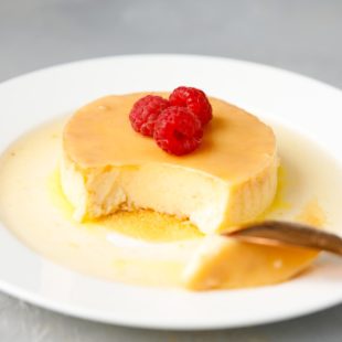 Keto Flan (creme Caramel) on a white plate, topped with raspberries