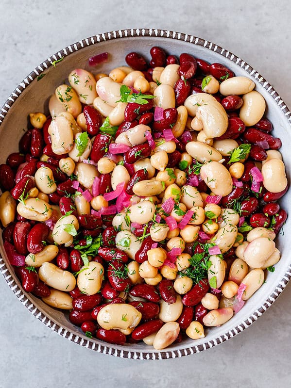 Easy three bean salad with kidney beans, cannellini, chickpeas, red onion and fresh herbs in a speckled bowl
