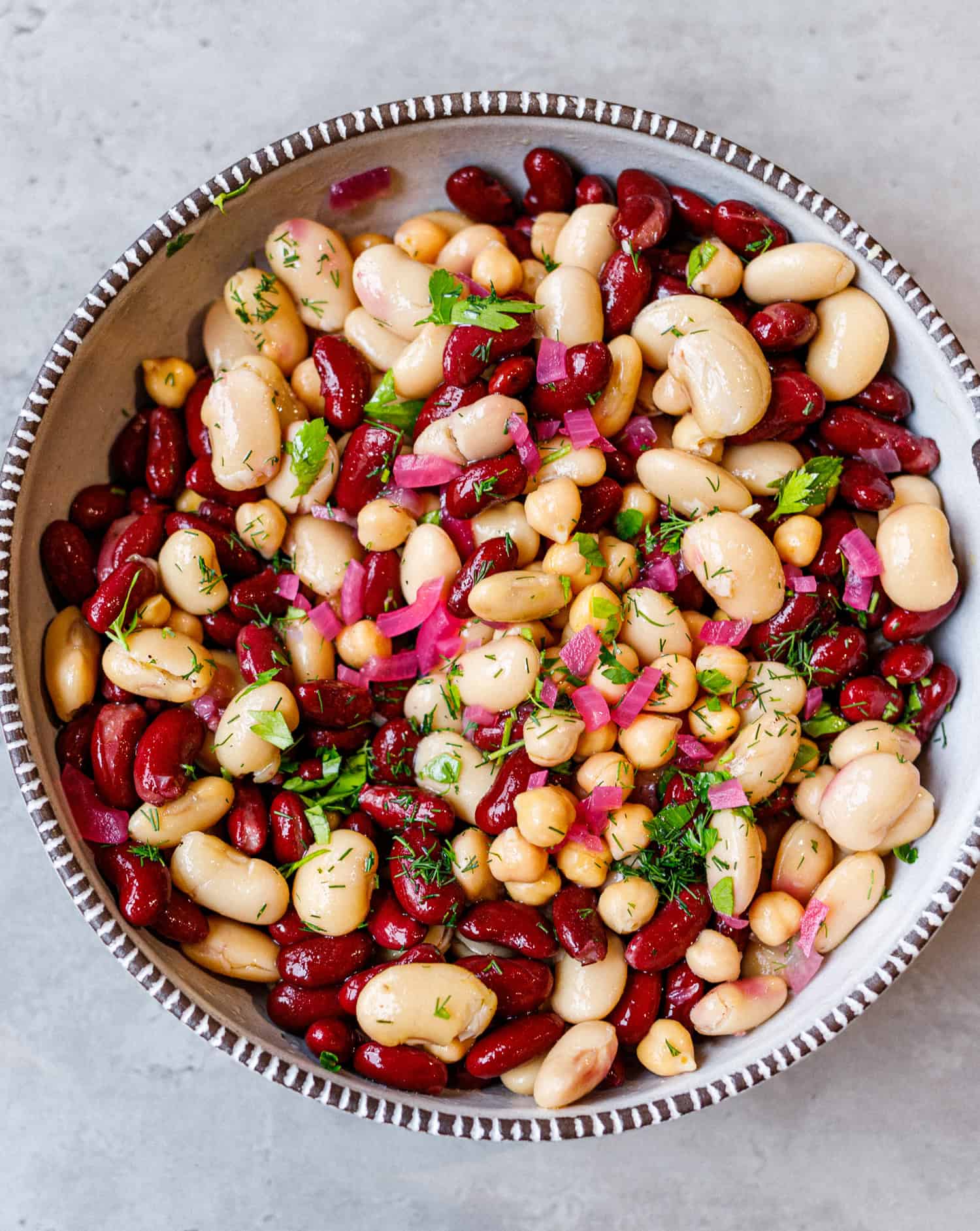 Easy three bean salad with kidney beans, cannellini, chickpeas, red onion and fresh herbs in a speckled bowl