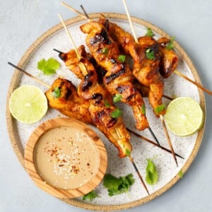 A plate with chicken Satay skewers on it