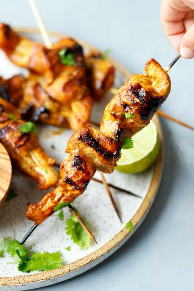 A hand holding a chicken Satay skewer