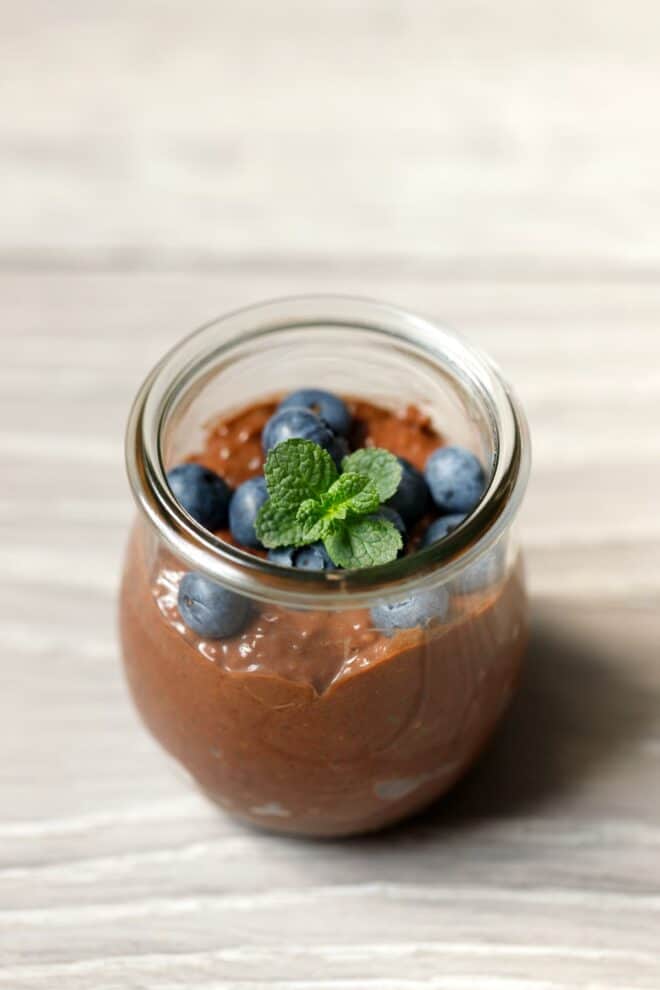 A glass jar with chocolate chia seed pudding, topped with berries