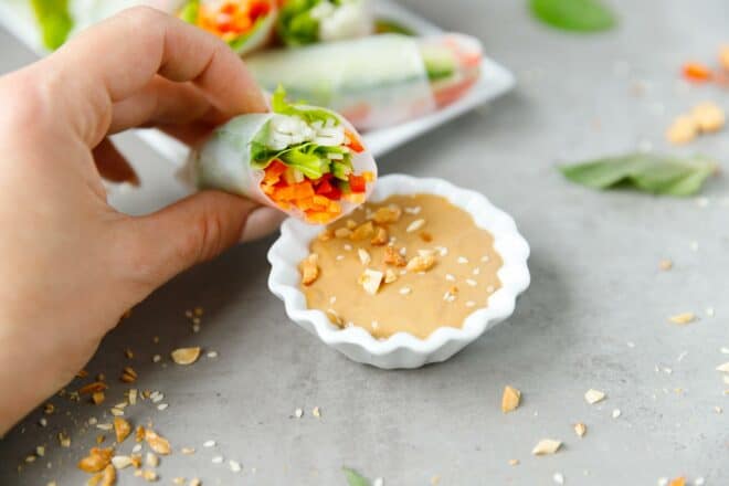 A hand dipping fresh spring roll into peanut butter sauce