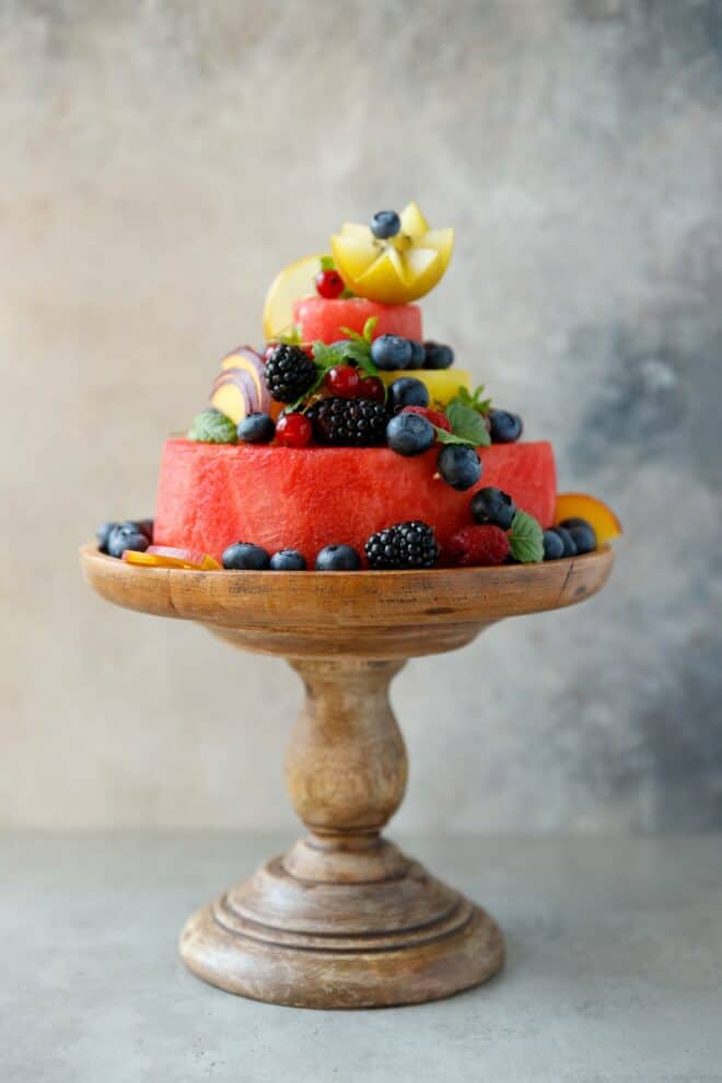 A two layer raw watermelon cake on a bamboo cake stand