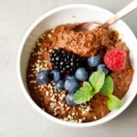 A white bowl with a spoon and creamy chocolate oat bran porridge inside