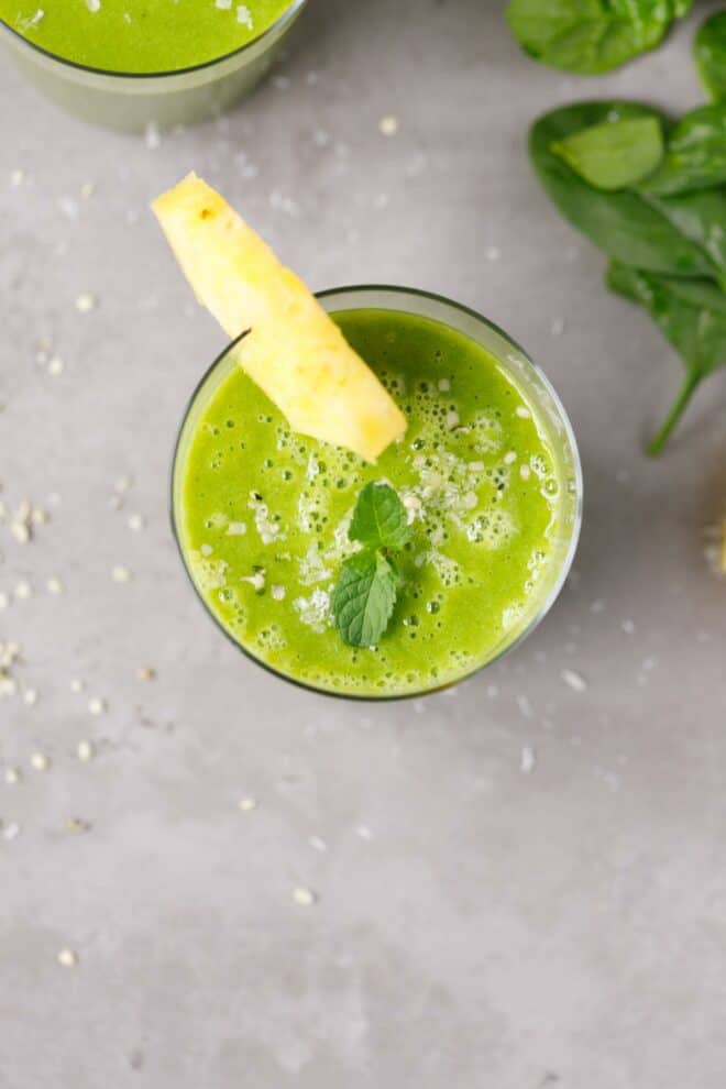 A small glass cup with green spinach pineapple smoothie and pineapple slice 