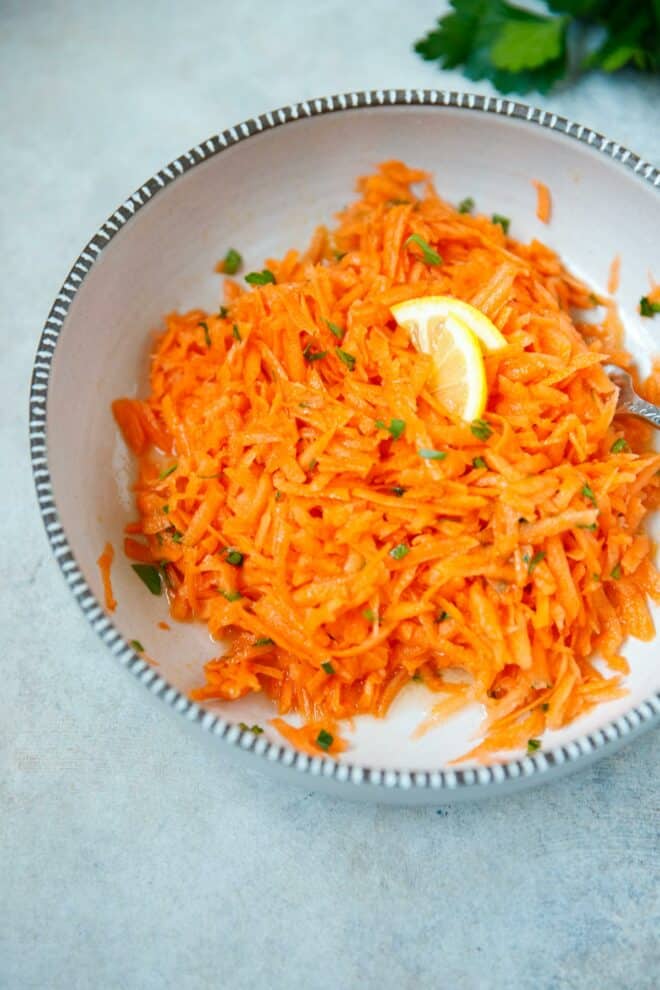 A bowl with grated carrot salad and lemon slices on top