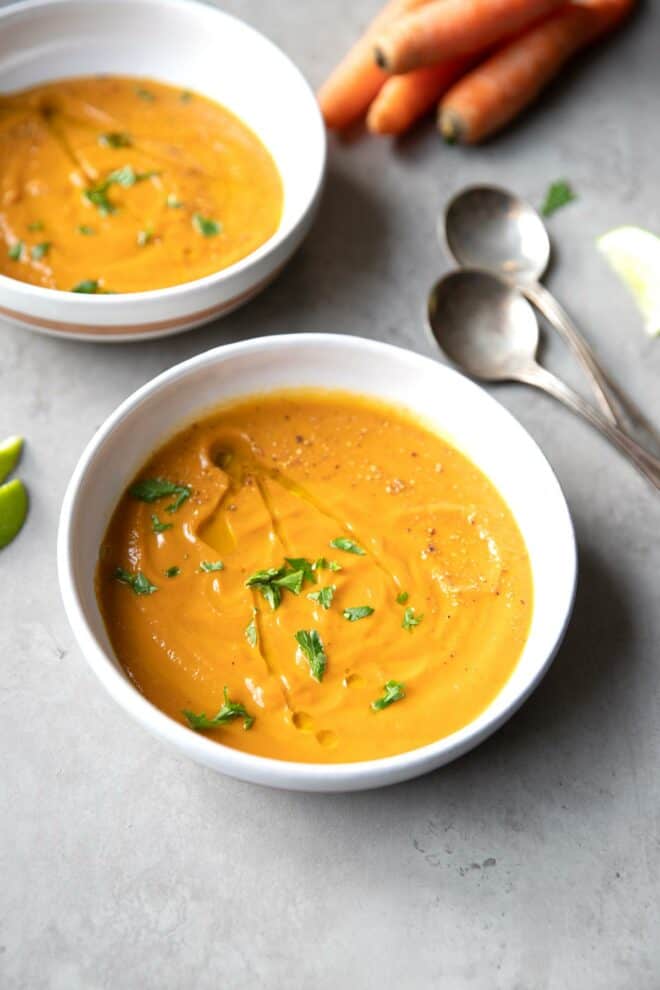 two bowls with carrot soup topped with parsley
