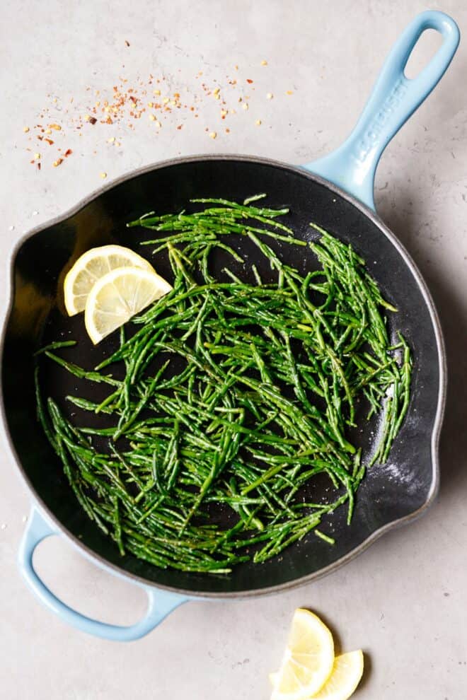 Sea asparagus with lemon slices in a cast iron pan