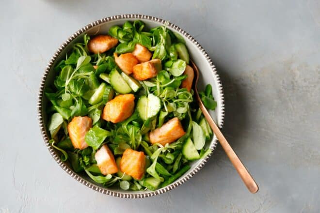 Lemon salad dressing over greens and salmon salad in a bowl