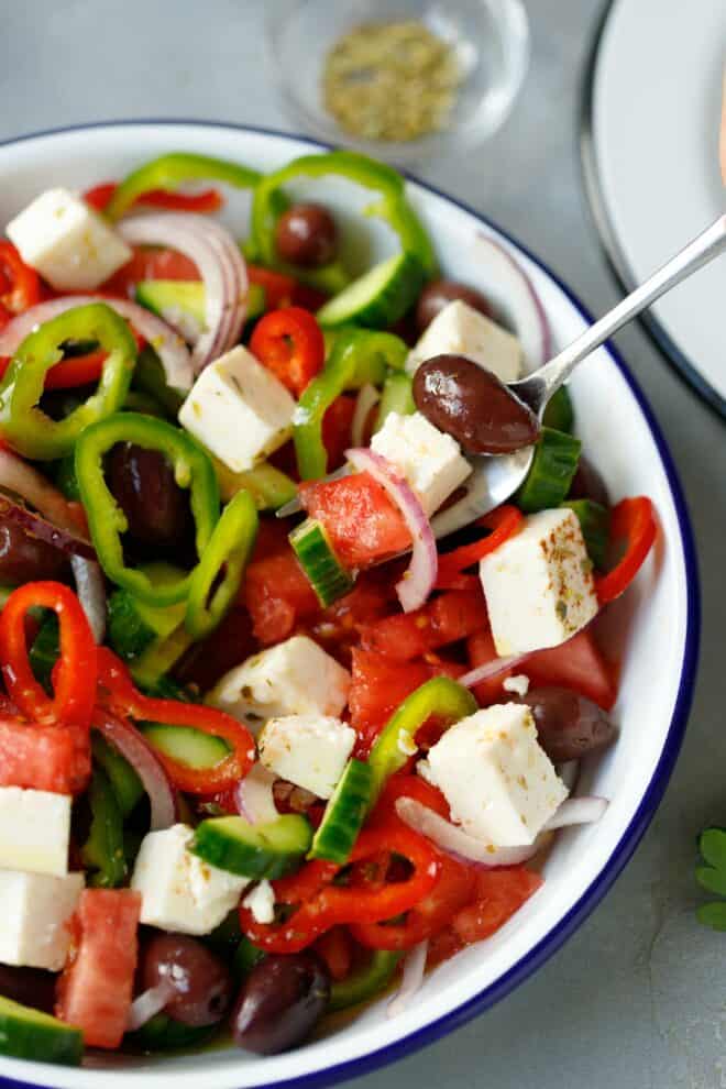Greek salad with Feta cheese in a bowl with dressing next to it