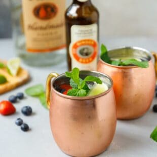 A copper mug with berry Moscow mule and ginger beer bottle behind.