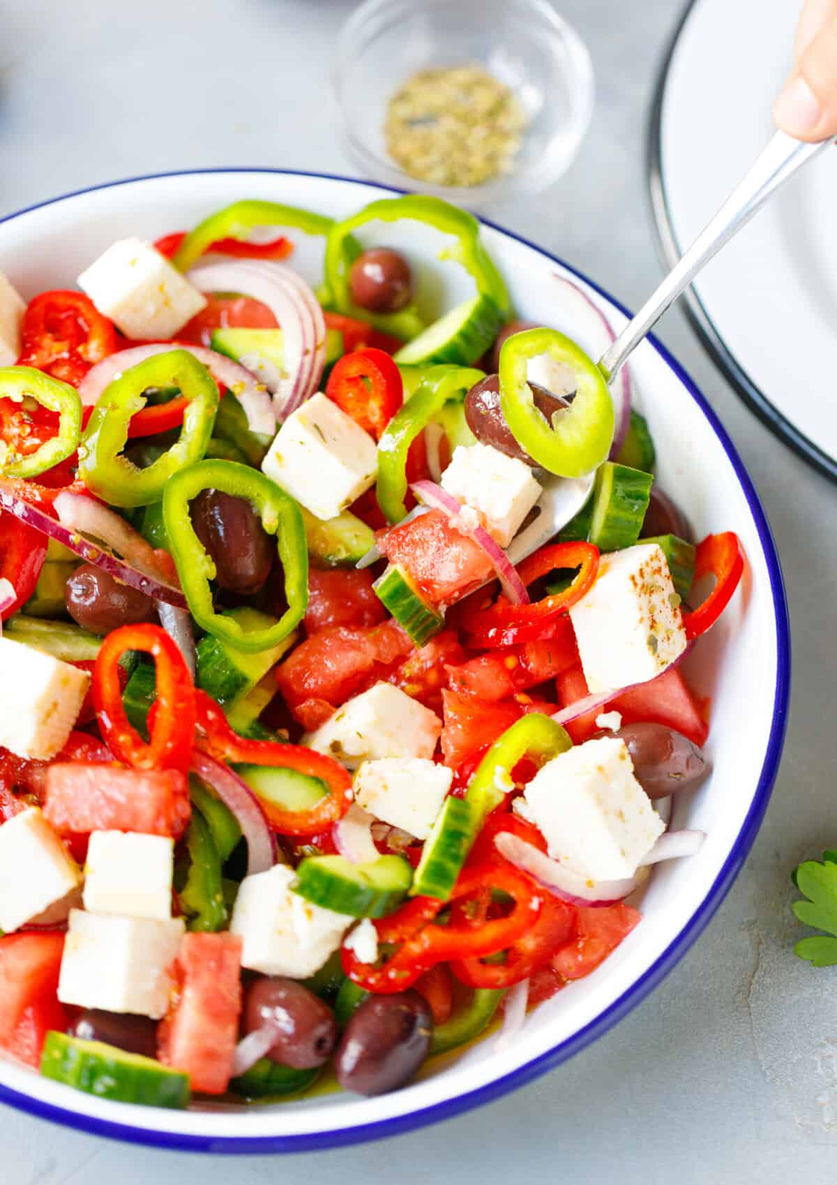 Mixing Greek salad with feta cheese, olives, cucumber, tomato and bell peppers in bowl