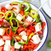 Mixing Greek salad with feta cheese, olives, cucumber, tomato and bell peppers in bowl