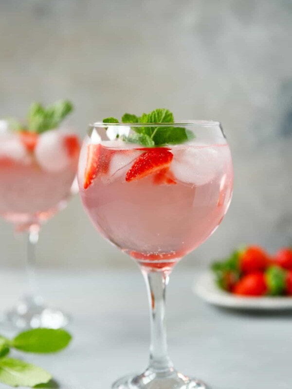 A gin baloon glass filled with pink strawberry gin and tonic cocktail