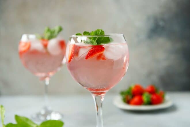Copa globo con gin tonic de fresa rosa, coronado con menta