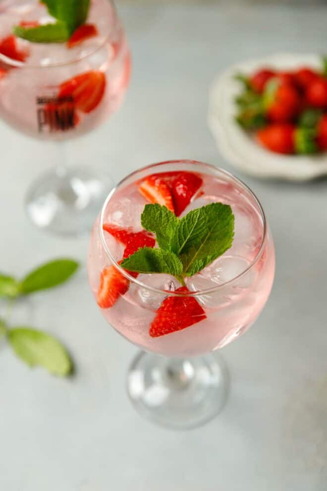 A cocktail glass/Copa glass filled with sliced strawberries, pink gin and tonic