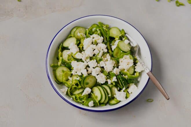 A bowl with cucumbers and peppers salad with feta on a gray countertop