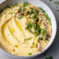 A ceramic bowl with yellow lentil hummus topped with herbs