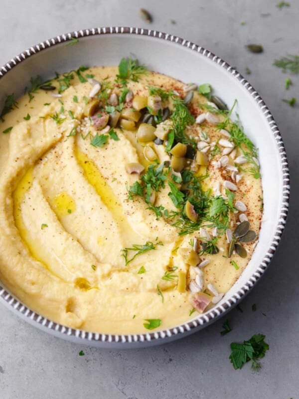 A ceramic bowl with yellow lentil hummus topped with herbs