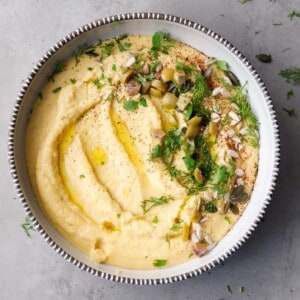 A bowl with yellow lentil dip, topped with herbs and seeds