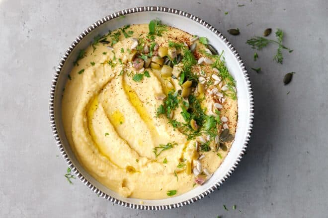 A bowl with Yellow lentil hummus dip on a gray countertop
