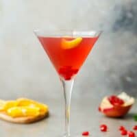 A glass with pomegranate martini and lemon peel
