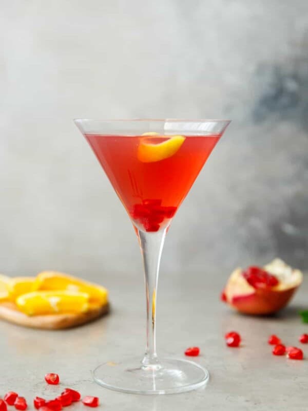 A glass with pomegranate martini and lemon peel