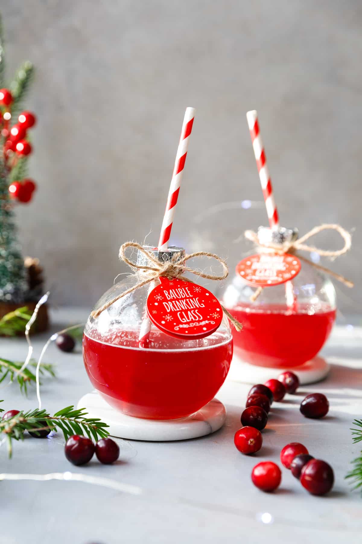 Two clear bauble glasses with cranberry gin and tonic cocktail and red and white paper straws