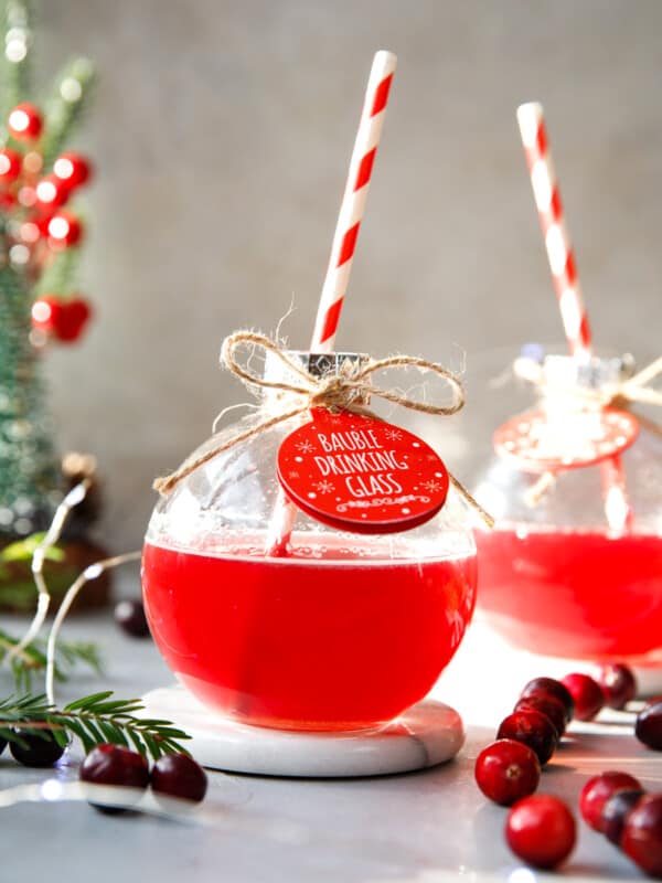 A bauble glass filled with cranberry gin and tonic cocktail with red and white paper straw