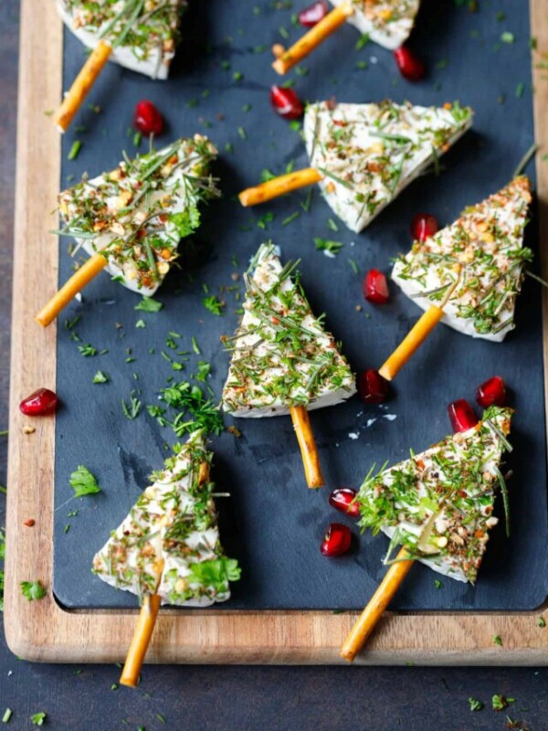 Cheese wedge herb covered Christmas trees on a chalk cutting board.