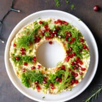 A white plate with Olivier salad wreath appetizer topped with chopped parsley and pomegranate seeds