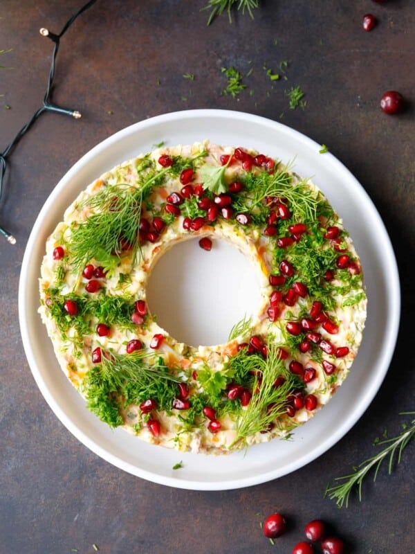A white plate with Olivier salad wreath appetizer topped with chopped parsley and pomegranate seeds