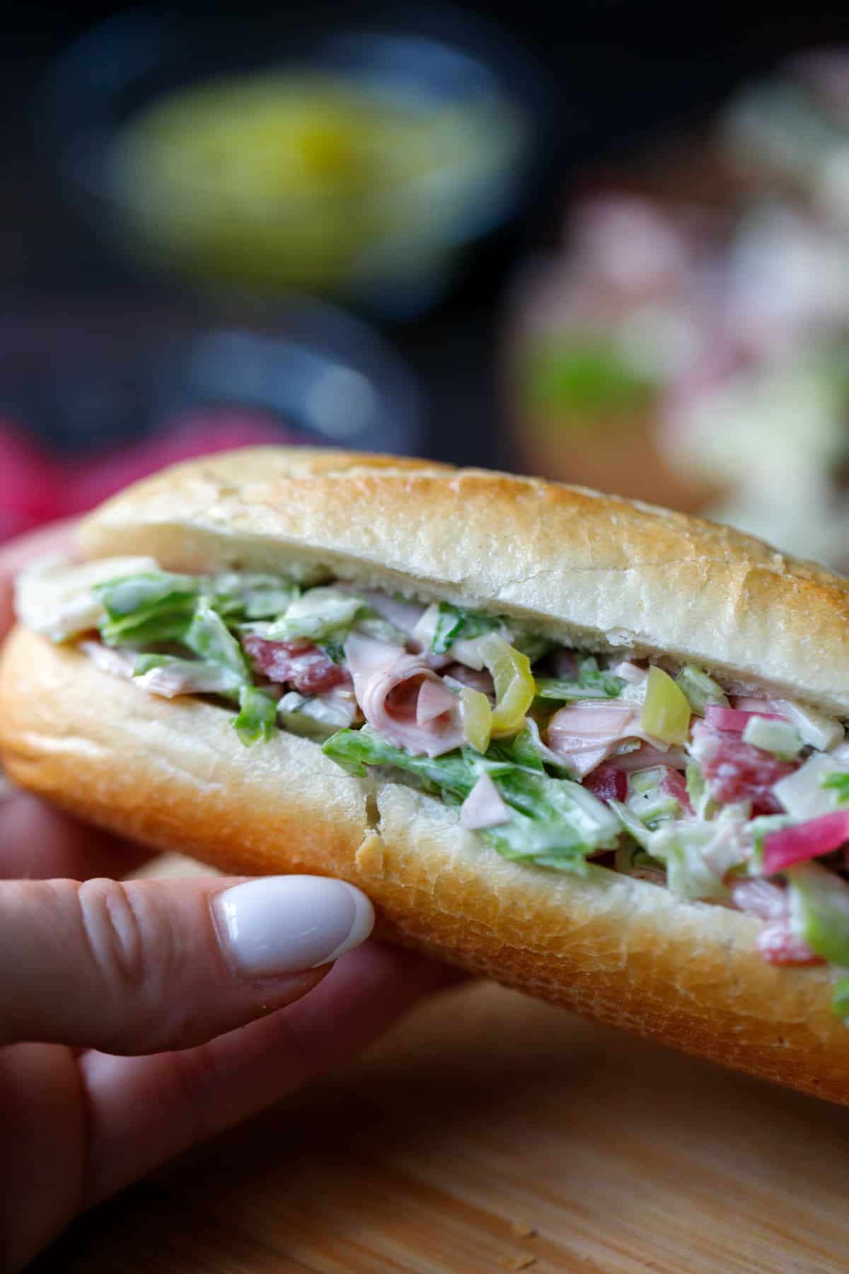 A hand holding a sub sandwich made with all chopped mortadella, salami, cheese, lettuce, tomatoes and mayo.