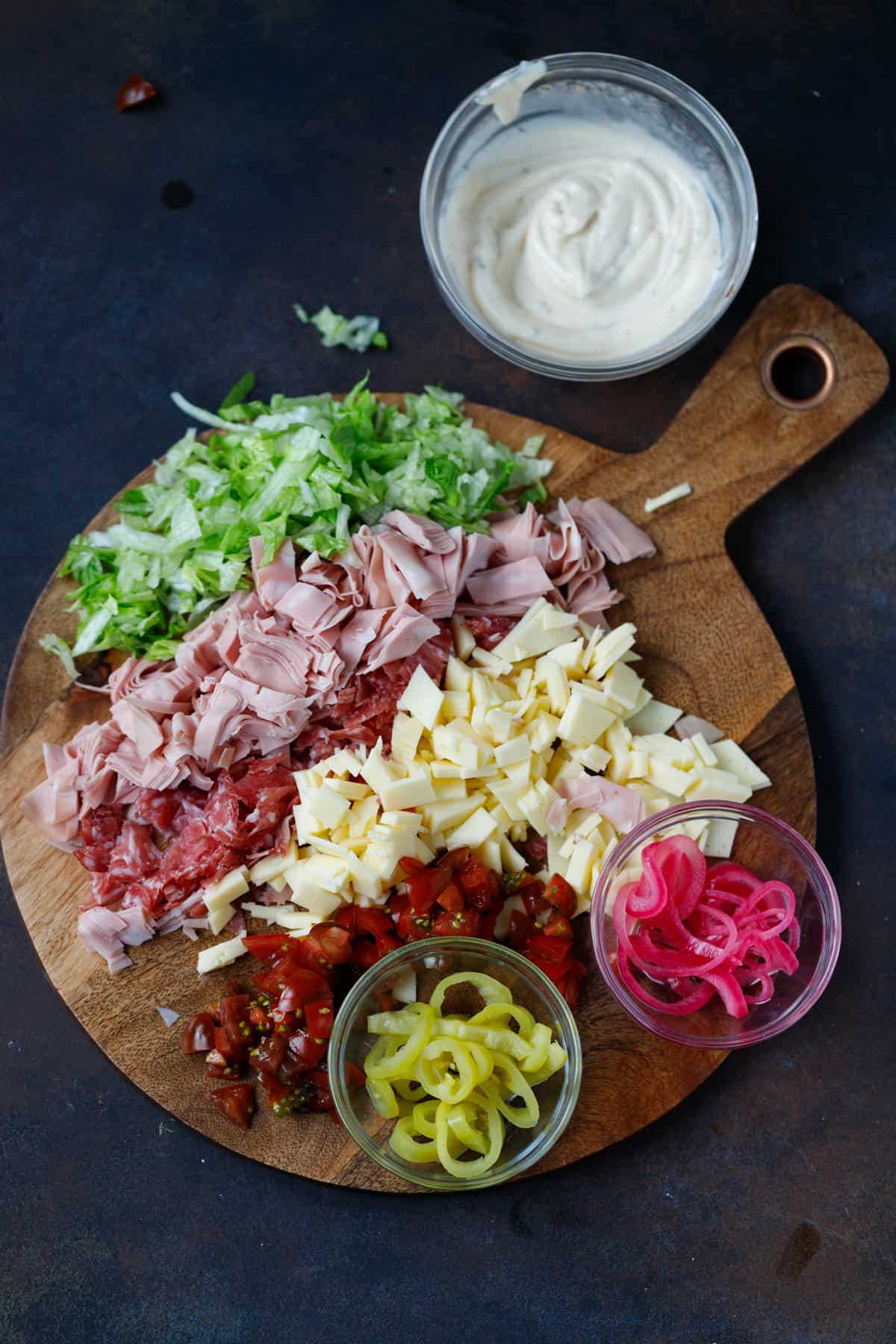 A cutting board with ingredients for chopped mortadella sub sandwich