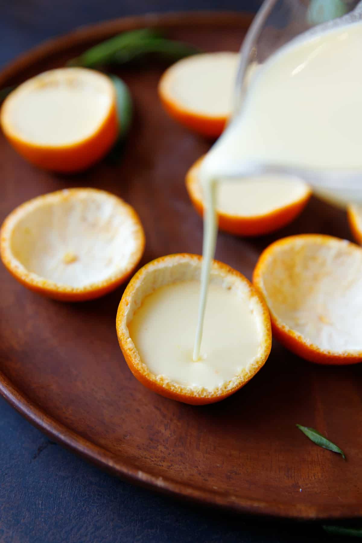 Tangerine shells on acacia plate filled with creamy posset mixture