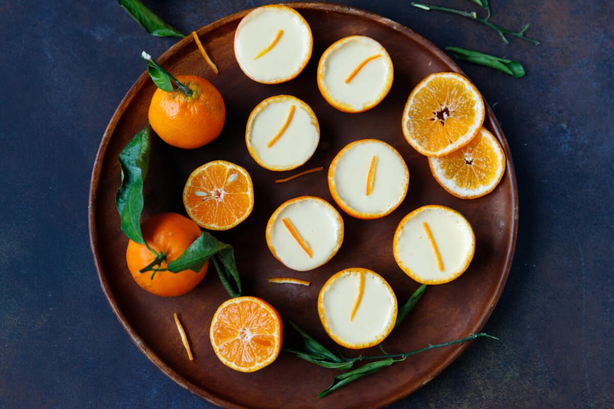 A wooden platter with tangerine posset inside tangerine shells