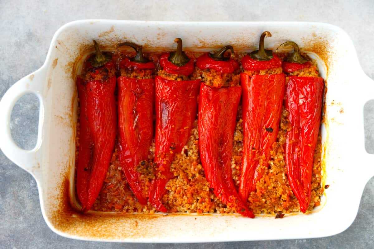 White ceramic baking dish with red bulgur stuffed peppers