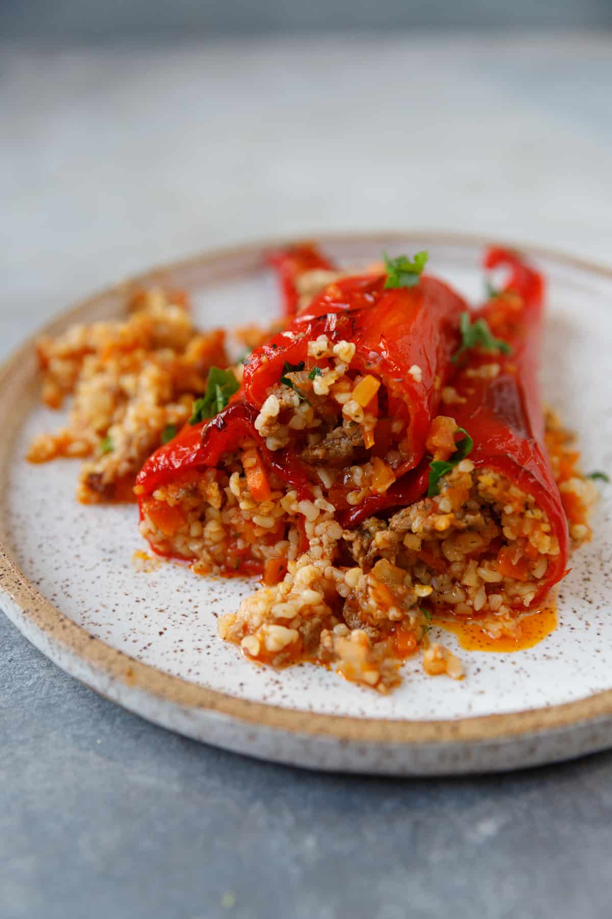 A plate with red peppers, stuffed with ground meat, veggies and bulhur