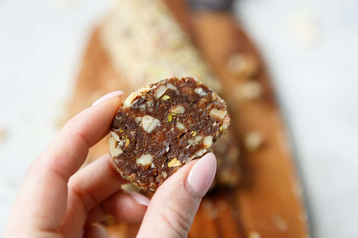 A hand holding a slice of Vegan Dat and Nut Roll