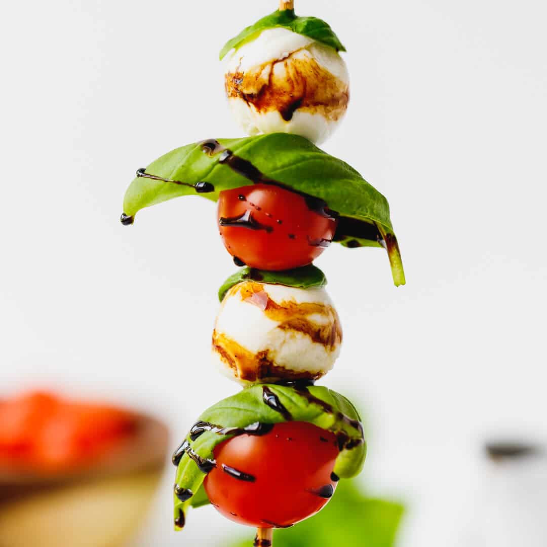 A hand holding caprese skewer - cherry tomatoes and baby mozzarella on a skick.